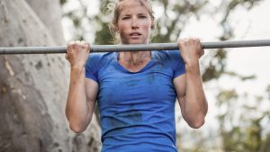 Fit woman performing pull-ups on bar during obstacle course